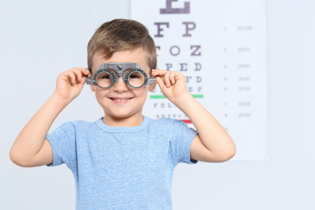 boy with trial frame beside eye chart