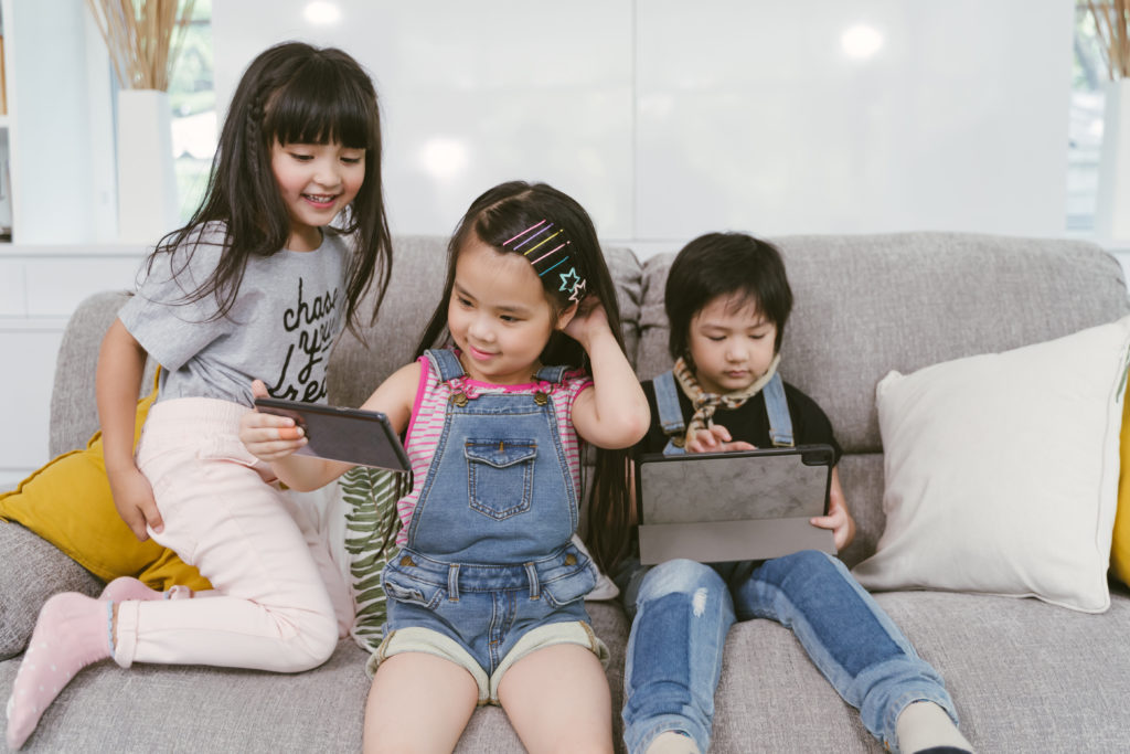group of little children watching film movie cartoons together on digital tablets and phones. Kids playing with smartphones with friends at home.