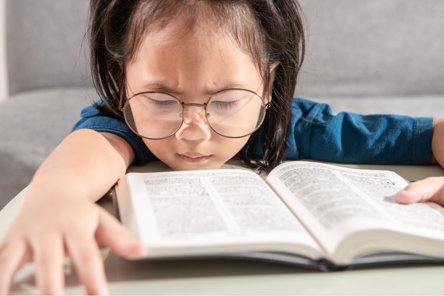 A kid with myopia trying to read a book with glasses